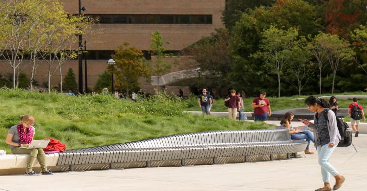 Students walk near a university building with lawn and trees.